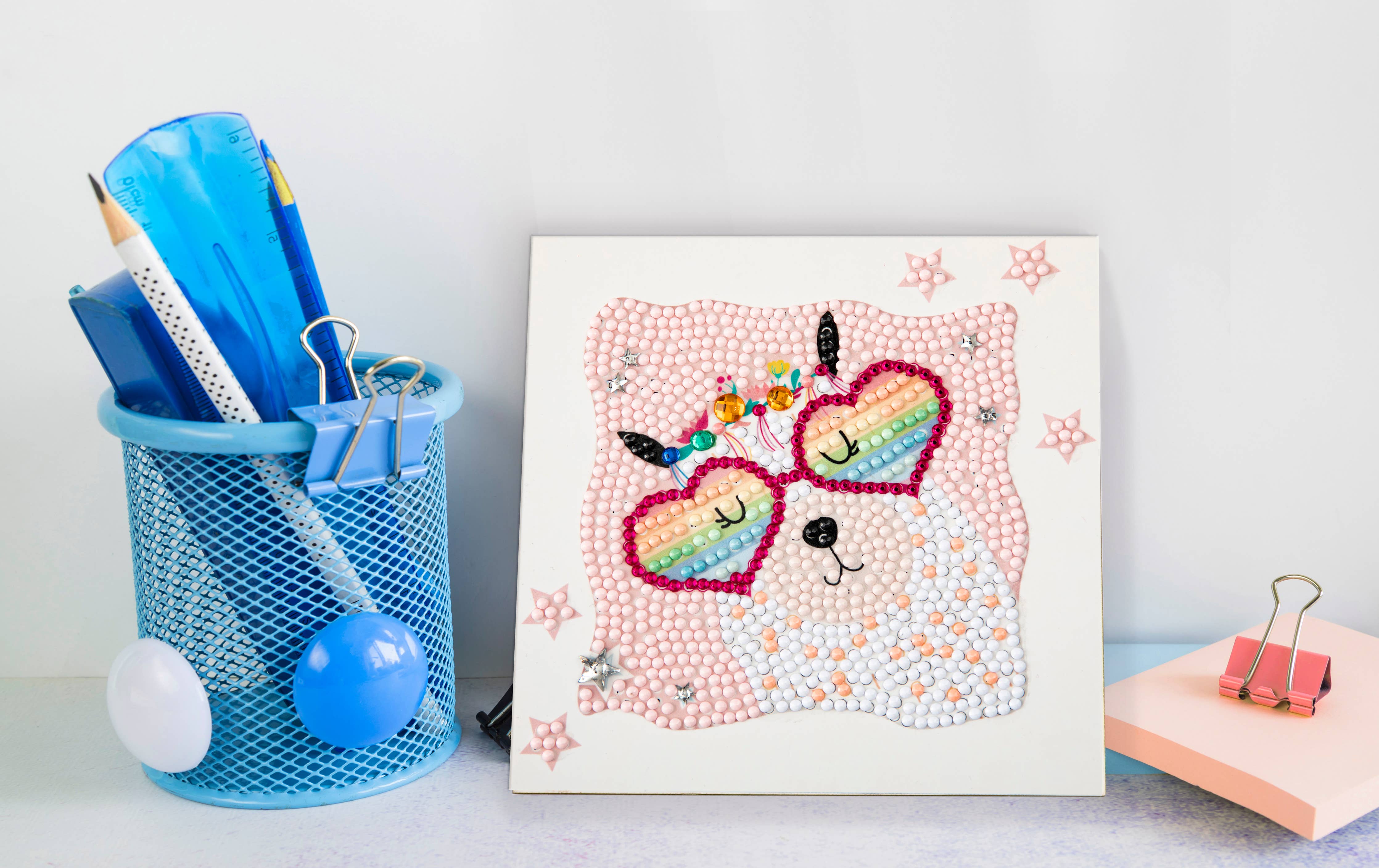 Colorful dot art of a cat with rainbow sunglasses on a white surface with stationery items.