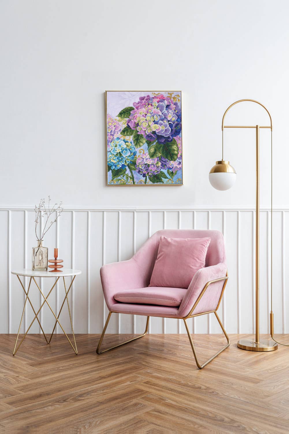 Pink armchair in a room with a floral painting, side table, and floor lamp.