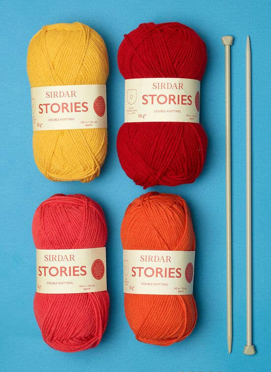Yarn balls, knitting needles, and a Sirdar Kith & Kin book on a blue background