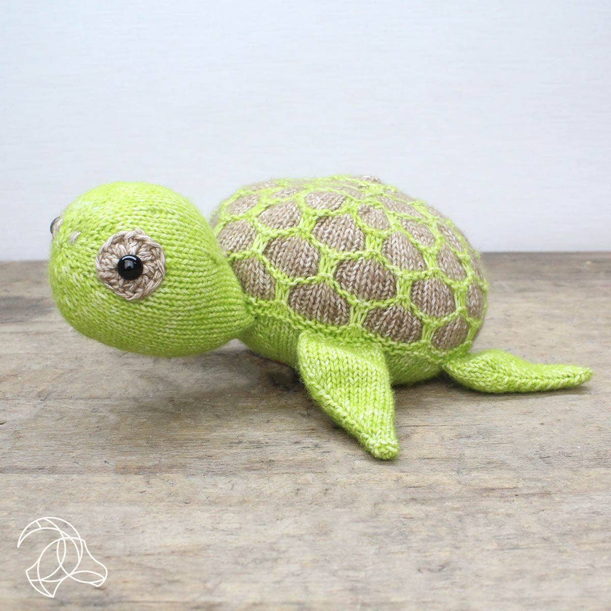Knitted turtle toy on a wooden surface with a light gray background