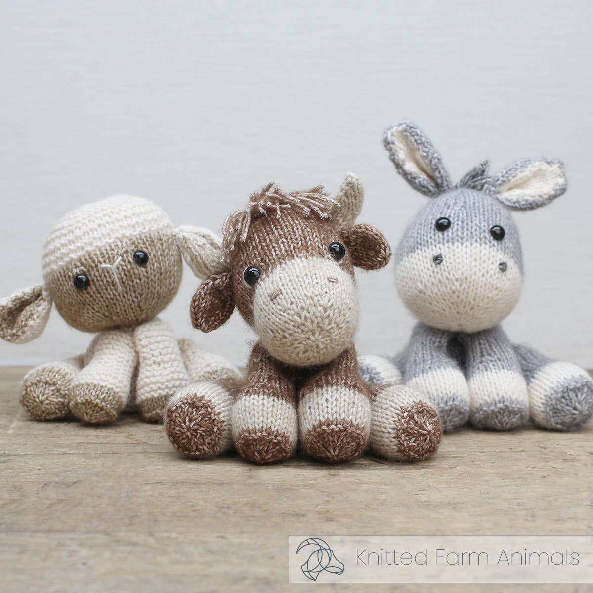 Three knitted farm animal toys (sheep, horse, donkey) on a wooden surface with a light background.