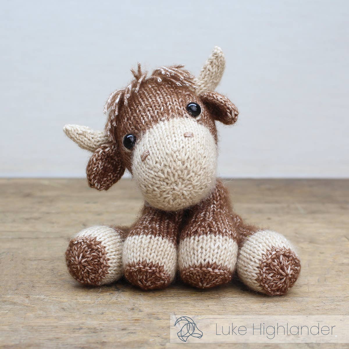 Knitted toy moose on a wooden surface with a light gray background