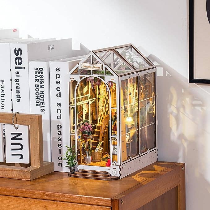 Decorative miniature greenhouse model on a wooden surface with books in the background