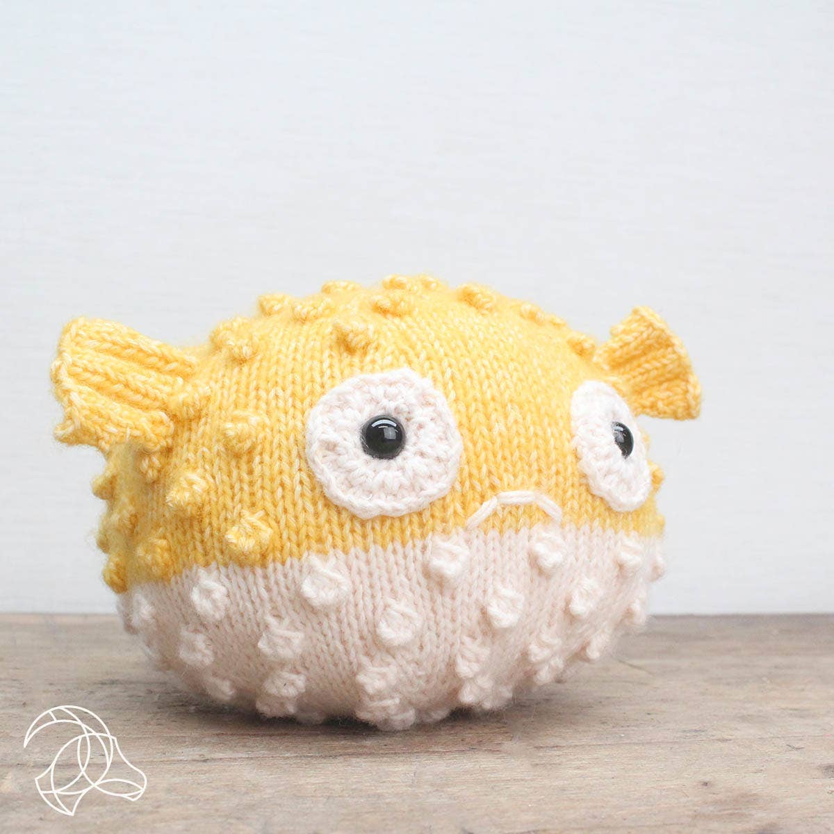 Knitted puffer fish toy on a wooden surface with a light gray background