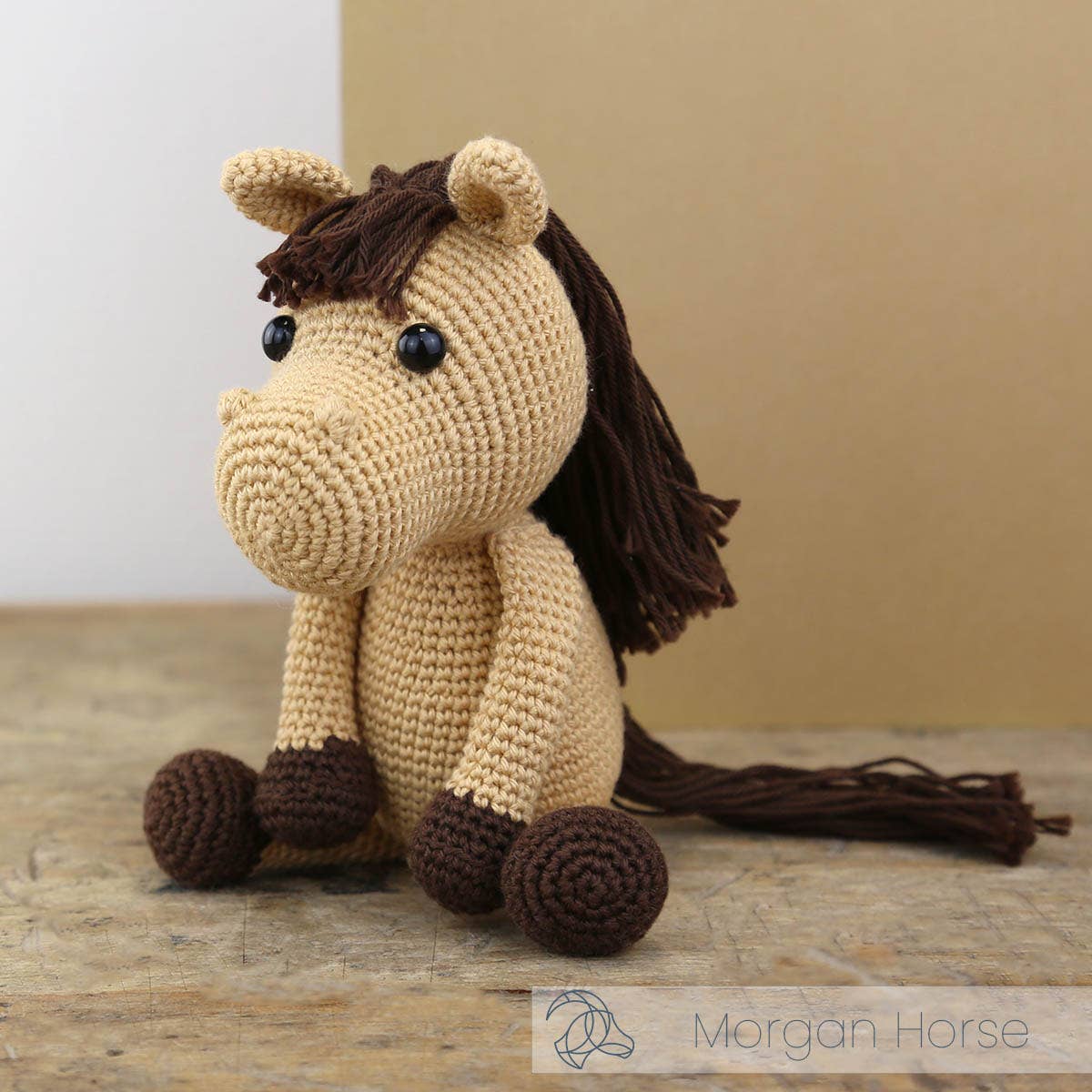 Crocheted horse toy with brown mane and feet on a wooden surface, brand 'Morgan Horse' visible.