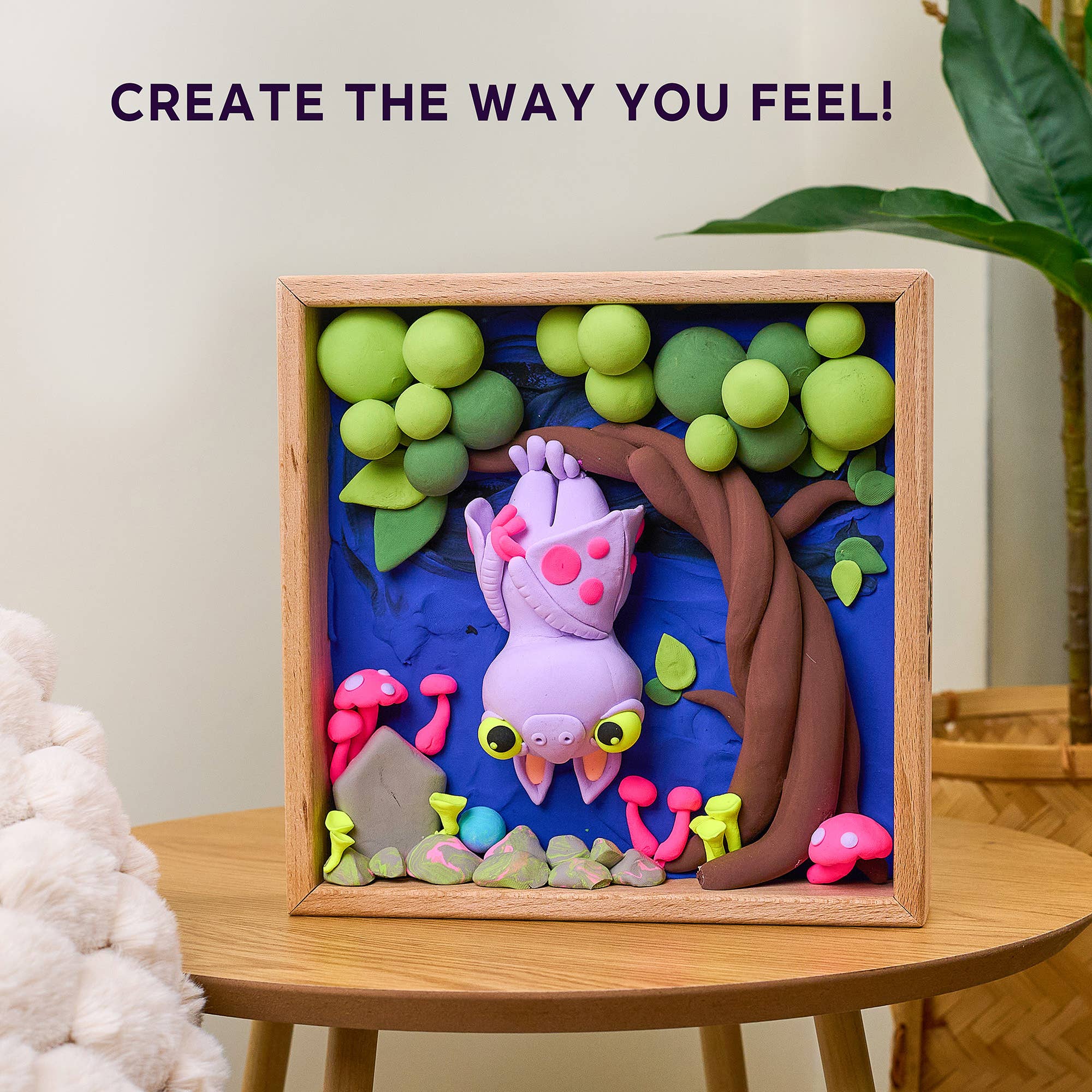 Colorful clay art of a creature in a wooden frame with text 'CREATE THE WAY YOU FEEL!' on a light background.