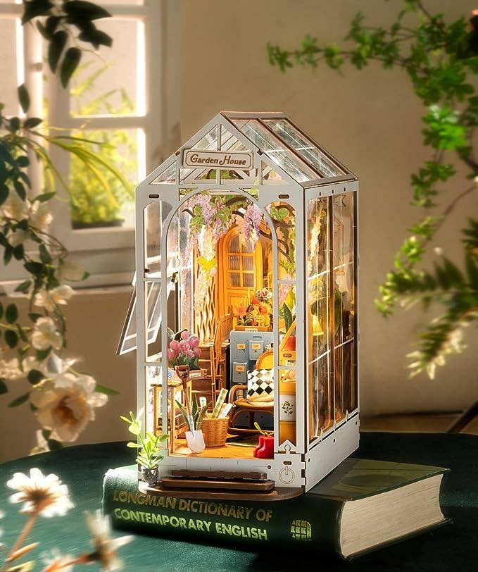 Miniature garden house model on a book with plants and flowers around