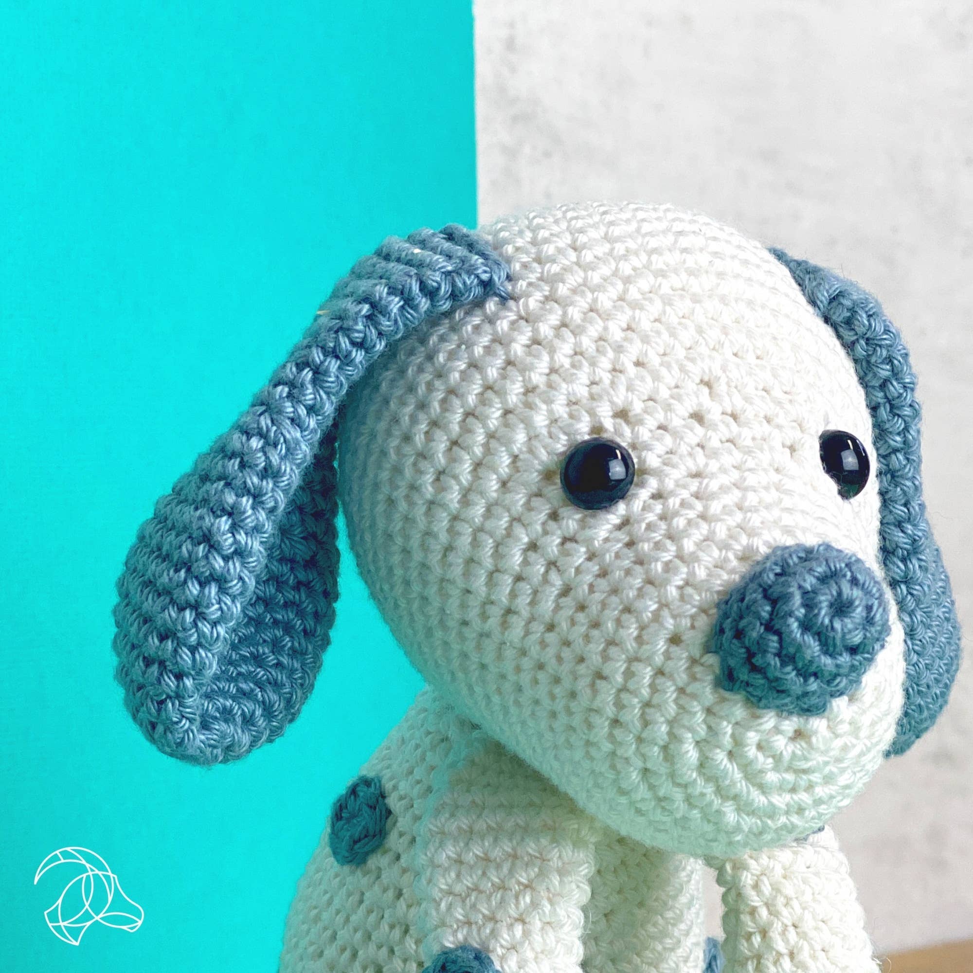 Crocheted dog toy with blue ears and nose against a teal background