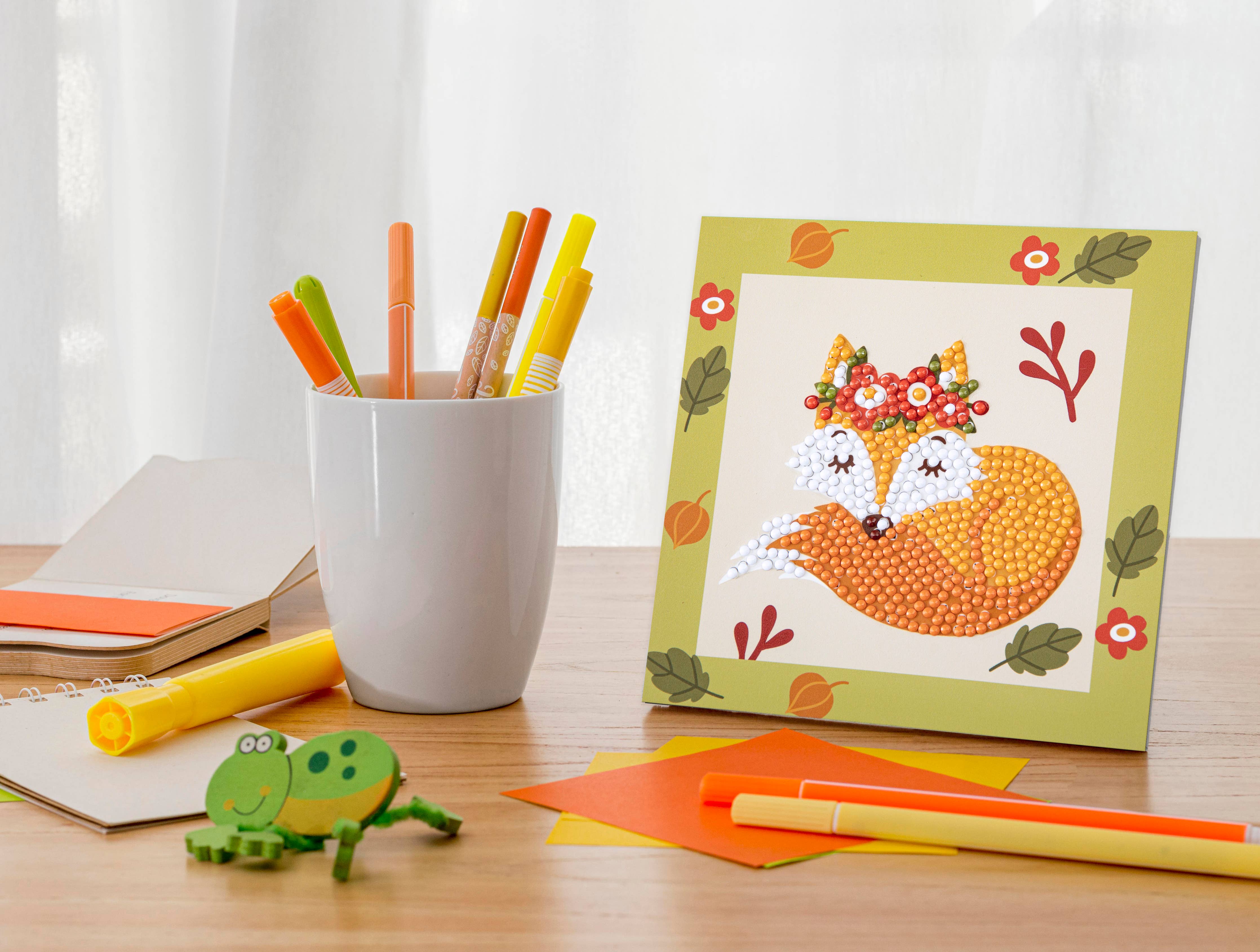 Desk with stationery items including colored pencils, a mug, and a card with a fox design.