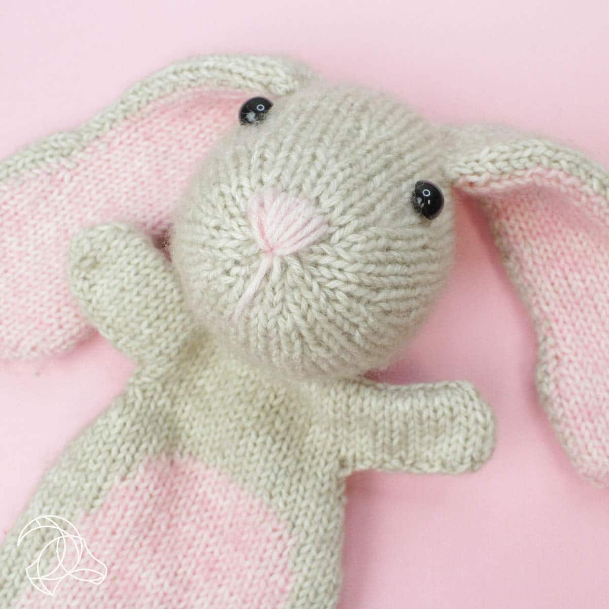 Knitted green bunny toy on a pink background
