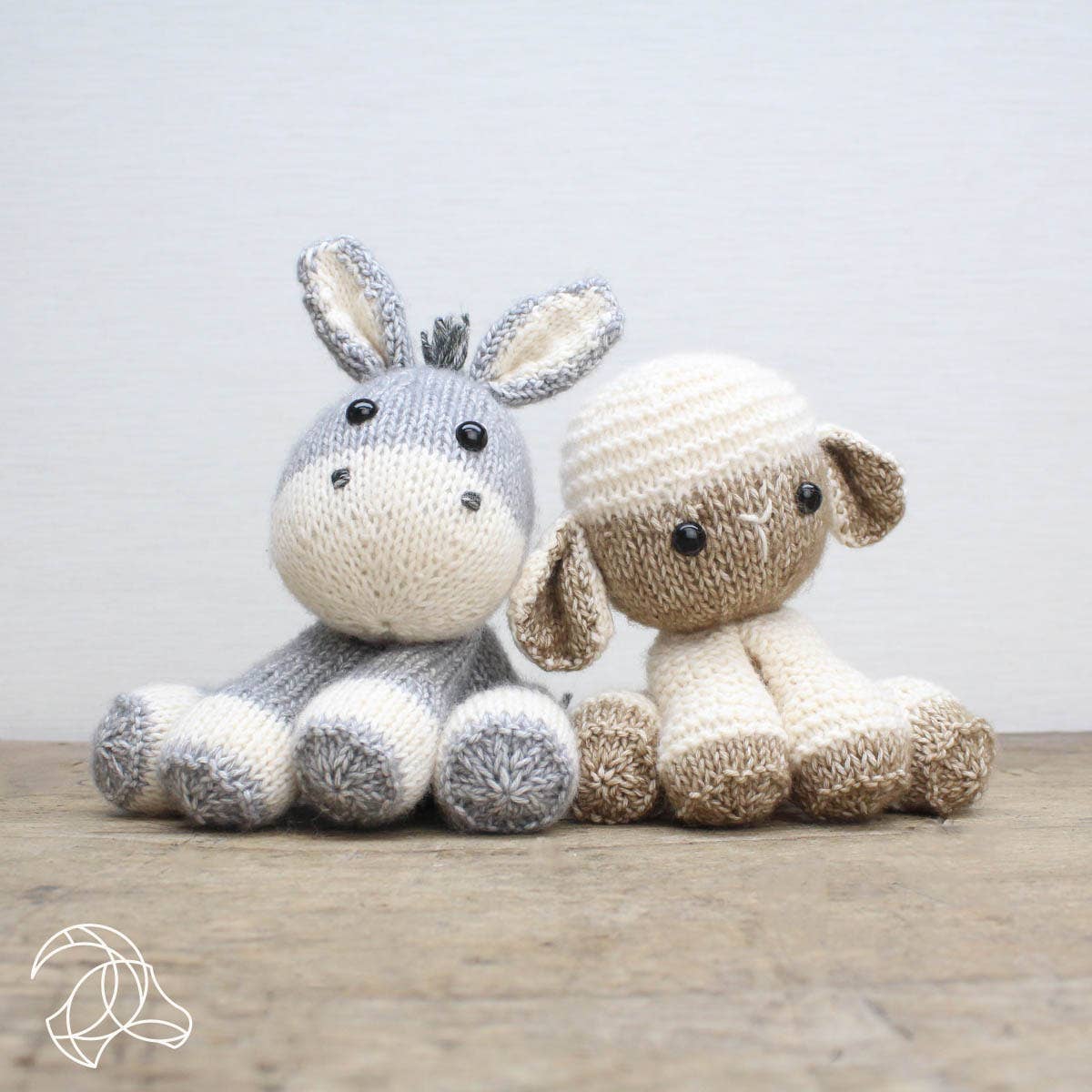 Knitted donkey and sheep toy sitting on a wooden surface with a light gray background