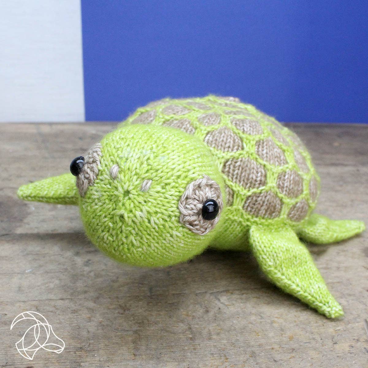 Knitted turtle toy on a wooden surface with a blue background