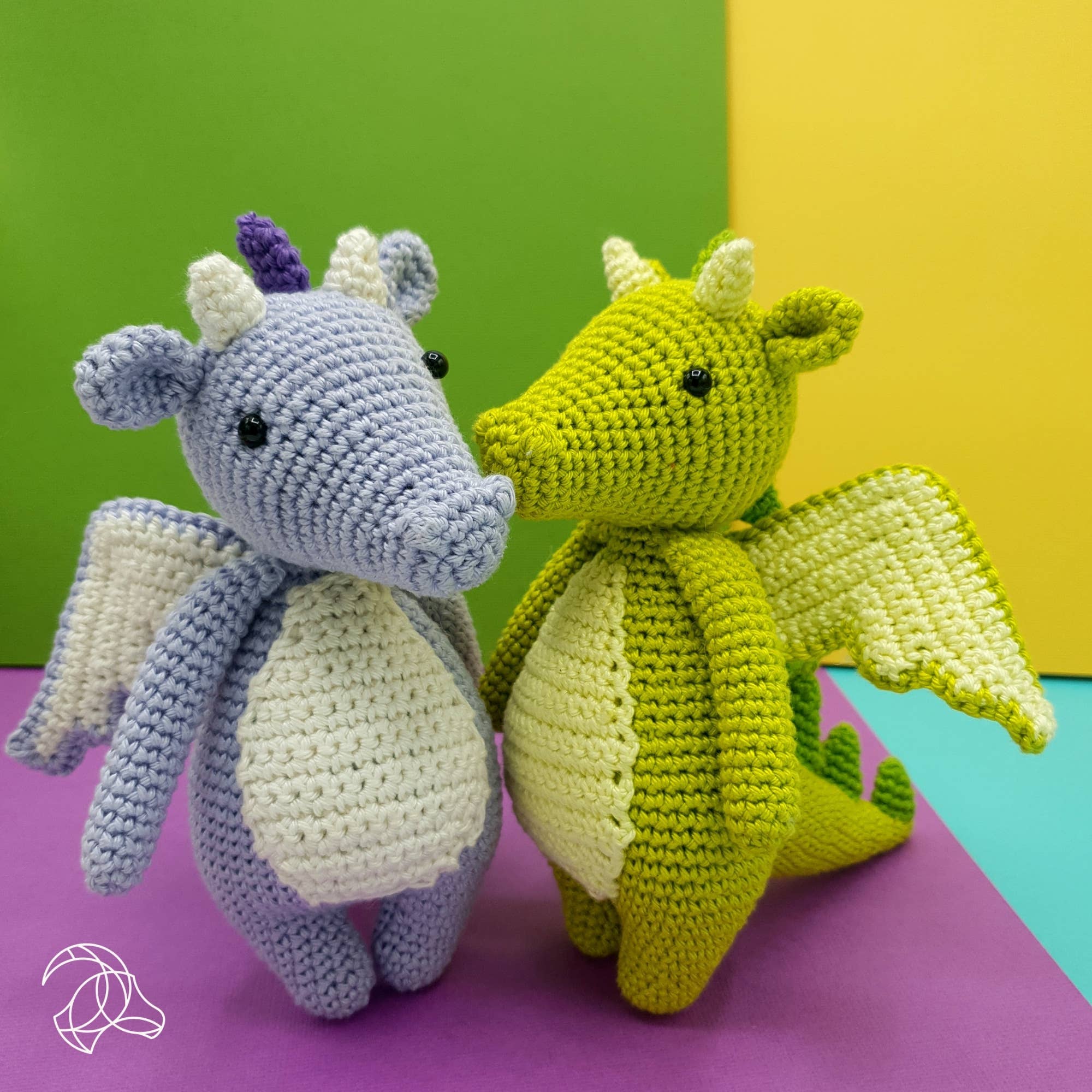 Two crocheted dragon toys, one purple and one green, on a colorful background.