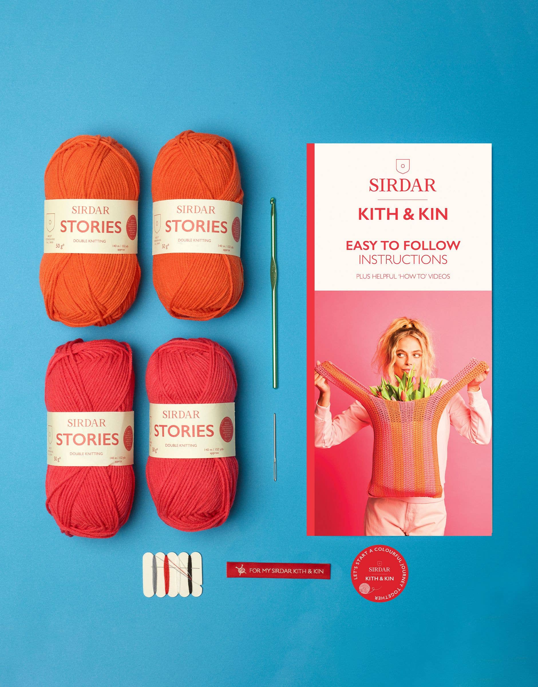 Red yarn balls and knitting needles with a Sirdar Kith & Kin book on a blue background