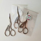 Three pairs of scissors on a white surface with a branded label.