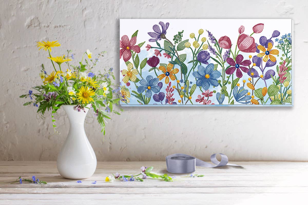 Colorful floral painting on a wall above a white vase with flowers and ribbon.