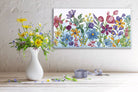 Colorful floral painting on a wall above a white vase with flowers and ribbon.
