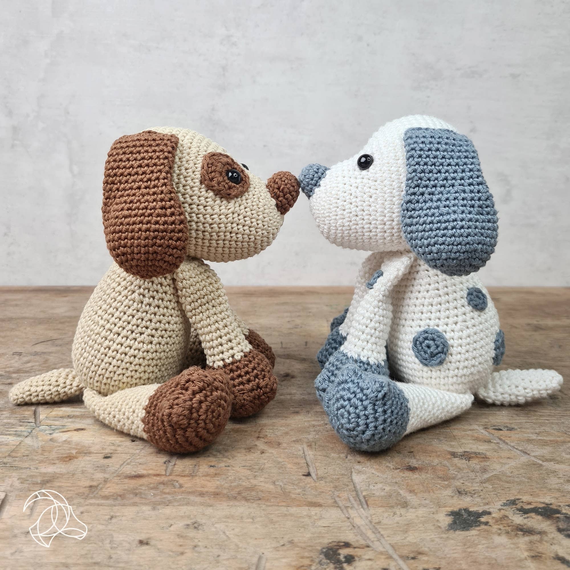 Two crocheted dog toys, one brown and one blue and white, on a wooden surface with a light gray background.