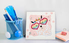 Colorful dot art of a cat with rainbow sunglasses on a white surface with stationery items.