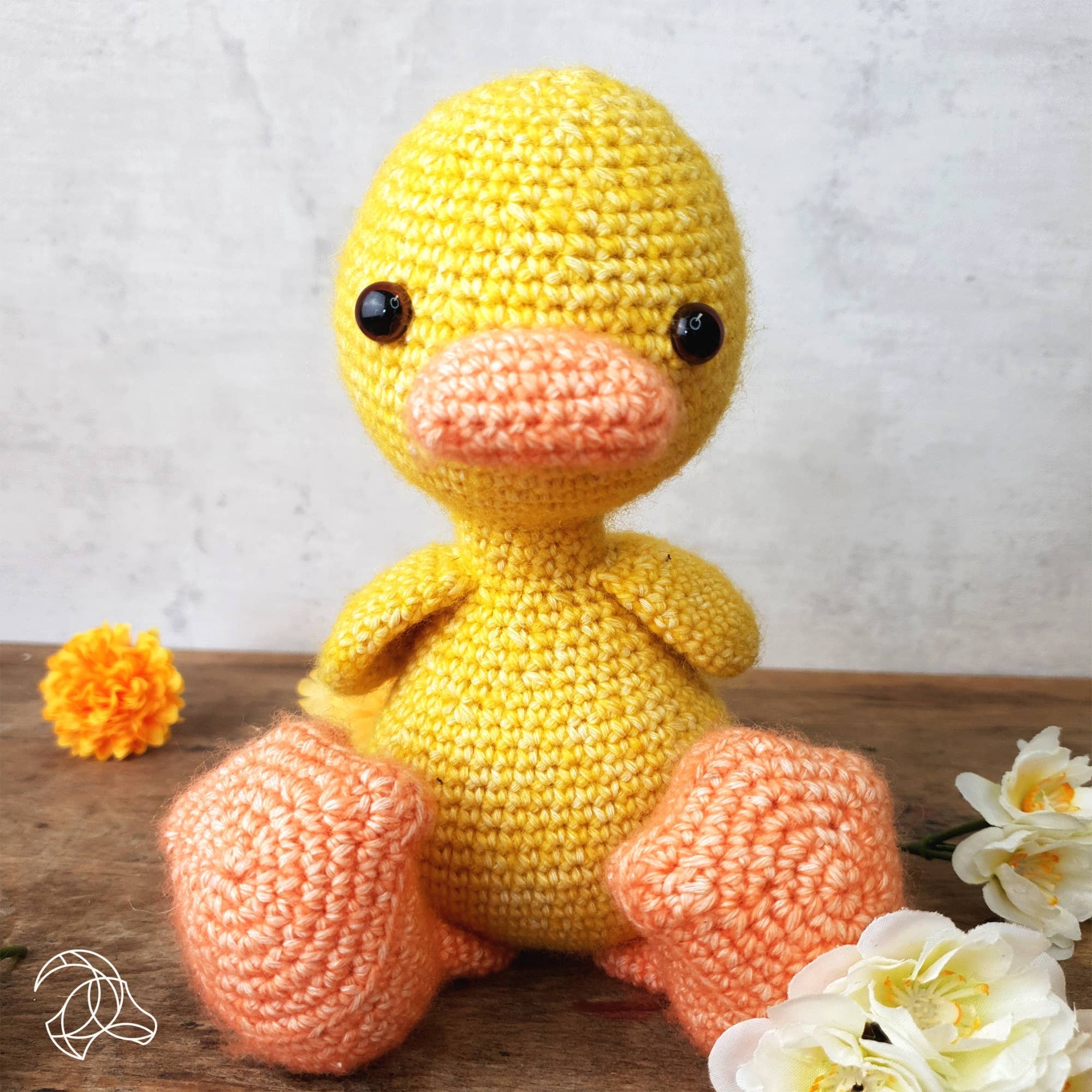 Crocheted yellow duck toy on a wooden surface with flowers.