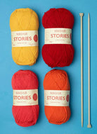 Yarn balls, knitting needles, and a Sirdar Kith & Kin book on a blue background