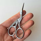 Hand holding a pair of small silver scissors against a plain background