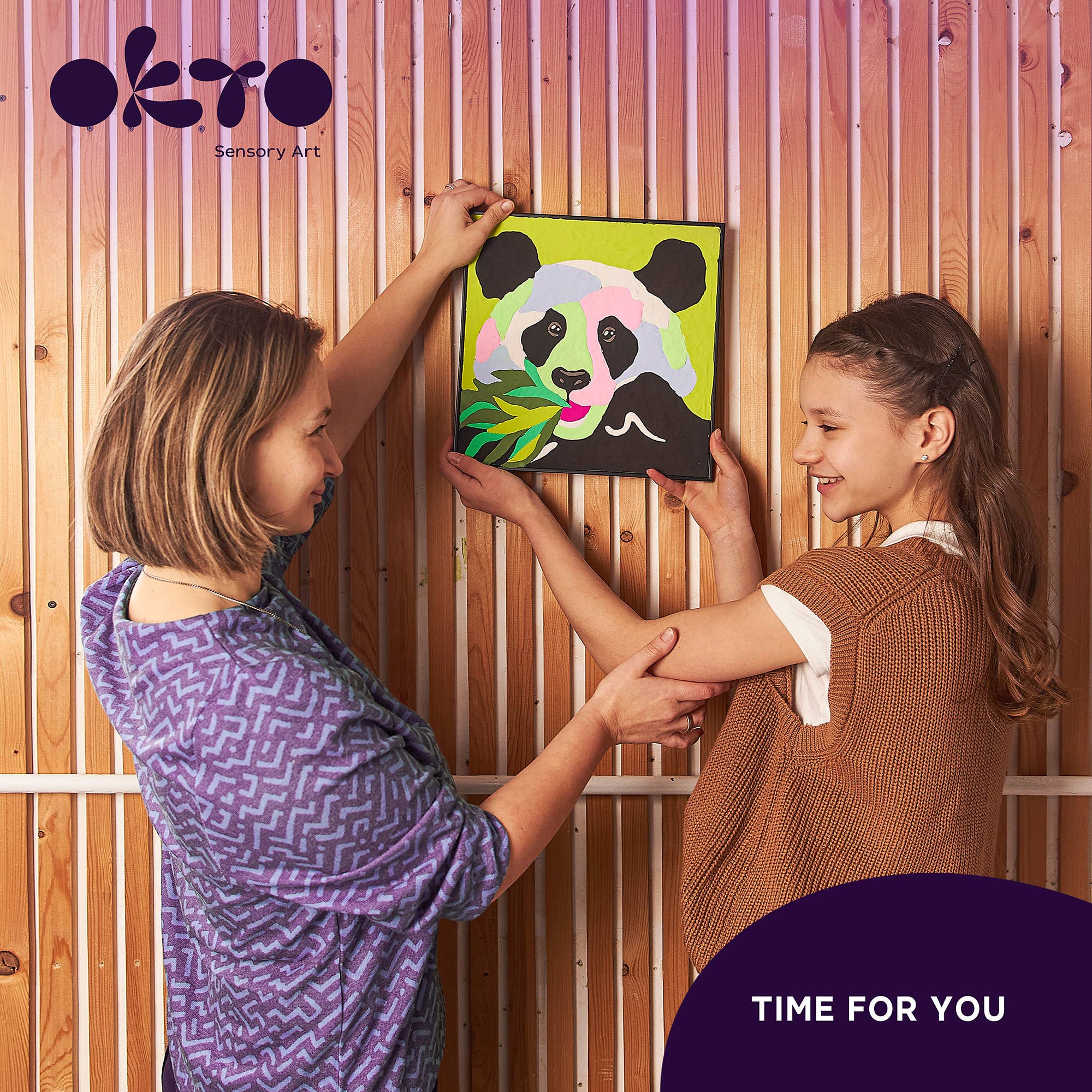 Two children holding a colorful painting of a panda against a wooden background with 'OKTO Sensory Art' branding.