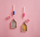 Two small scoops with colorful handles on a pink background