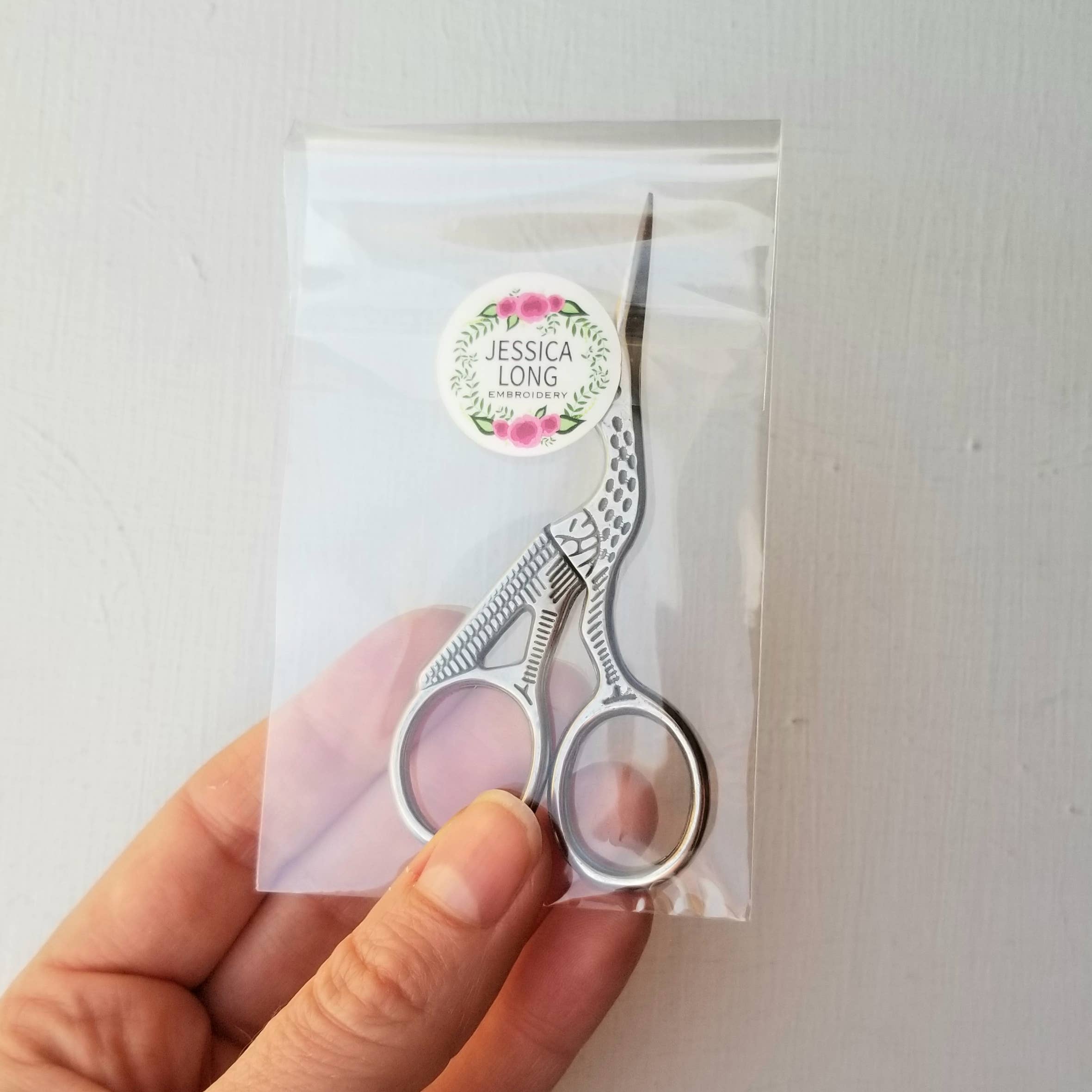 Small scissors held by a hand with a clear plastic bag featuring a 'Jessica Long' label.