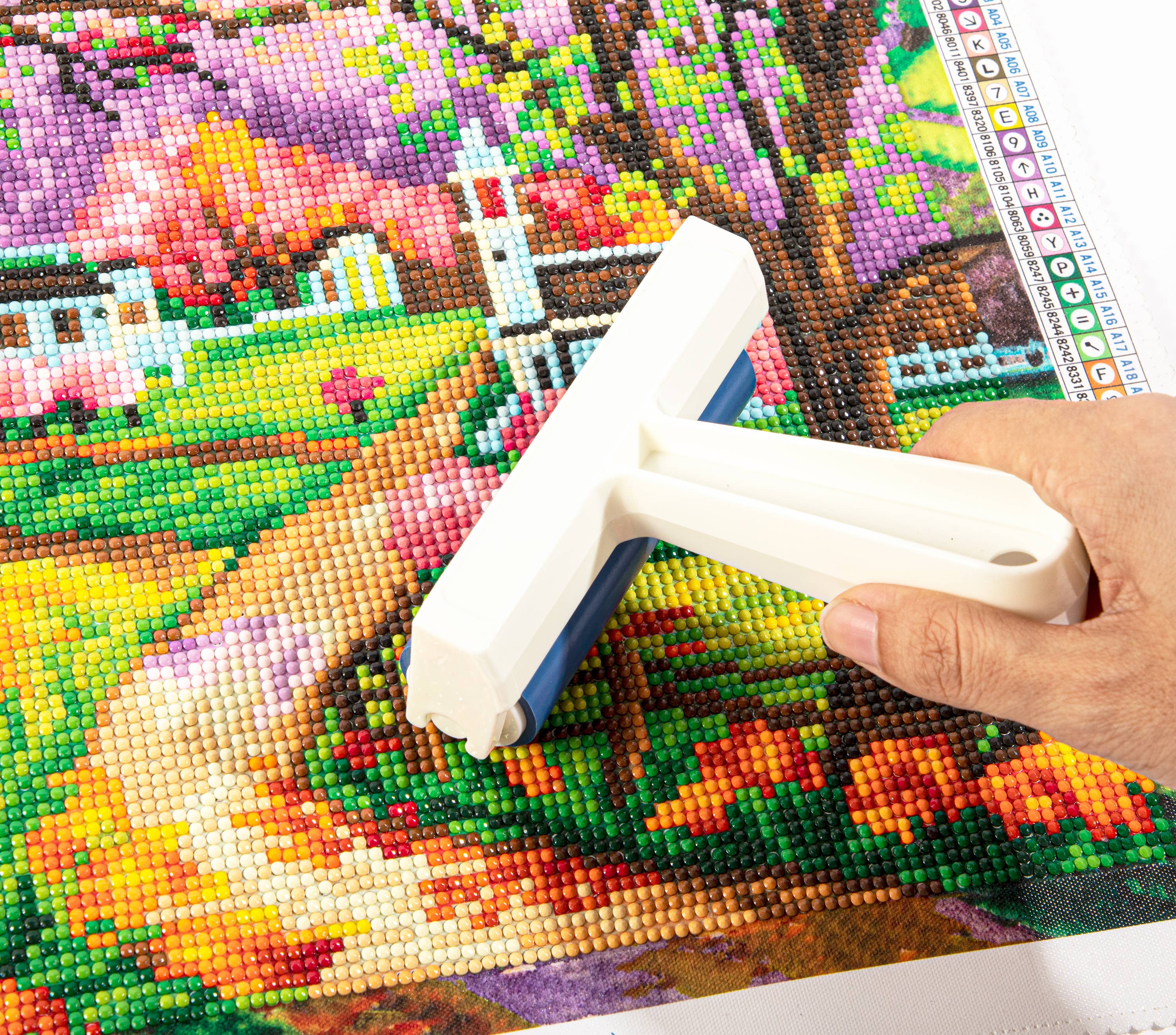 Hand using a tool on a partially completed diamond painting project