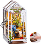 Miniature garden house model with open door, interior details, and a hand interacting with a small lever.