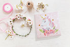 Card with unicorn design surrounded by flowers and ribbons on a white background