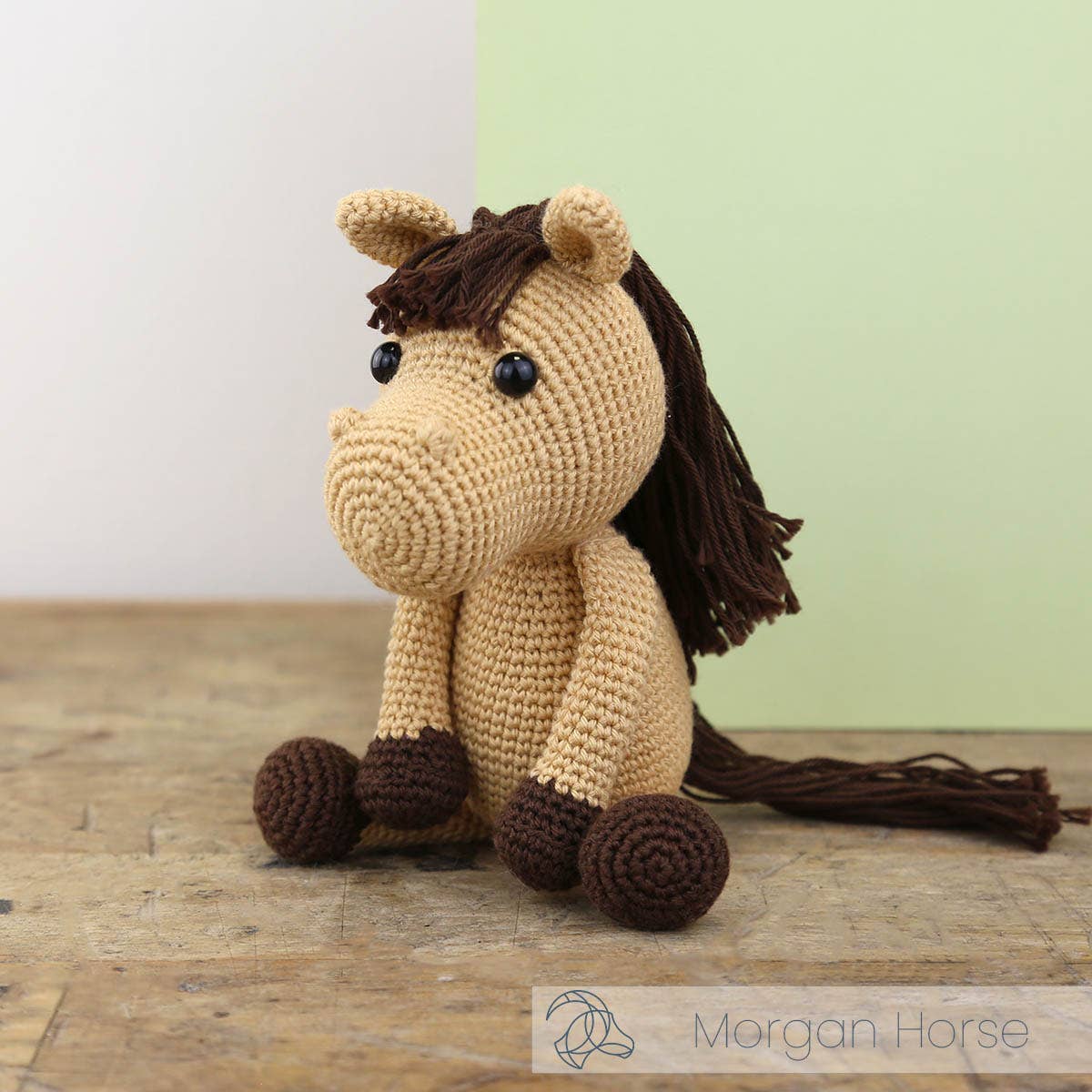 Crocheted horse toy with brown mane and tail on a wooden surface, brand 'Morgan Horse' visible.