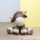 Knitted toy cow on a wooden surface with a light gray and yellow background