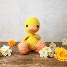 Crocheted yellow duck toy on a wooden surface with flowers