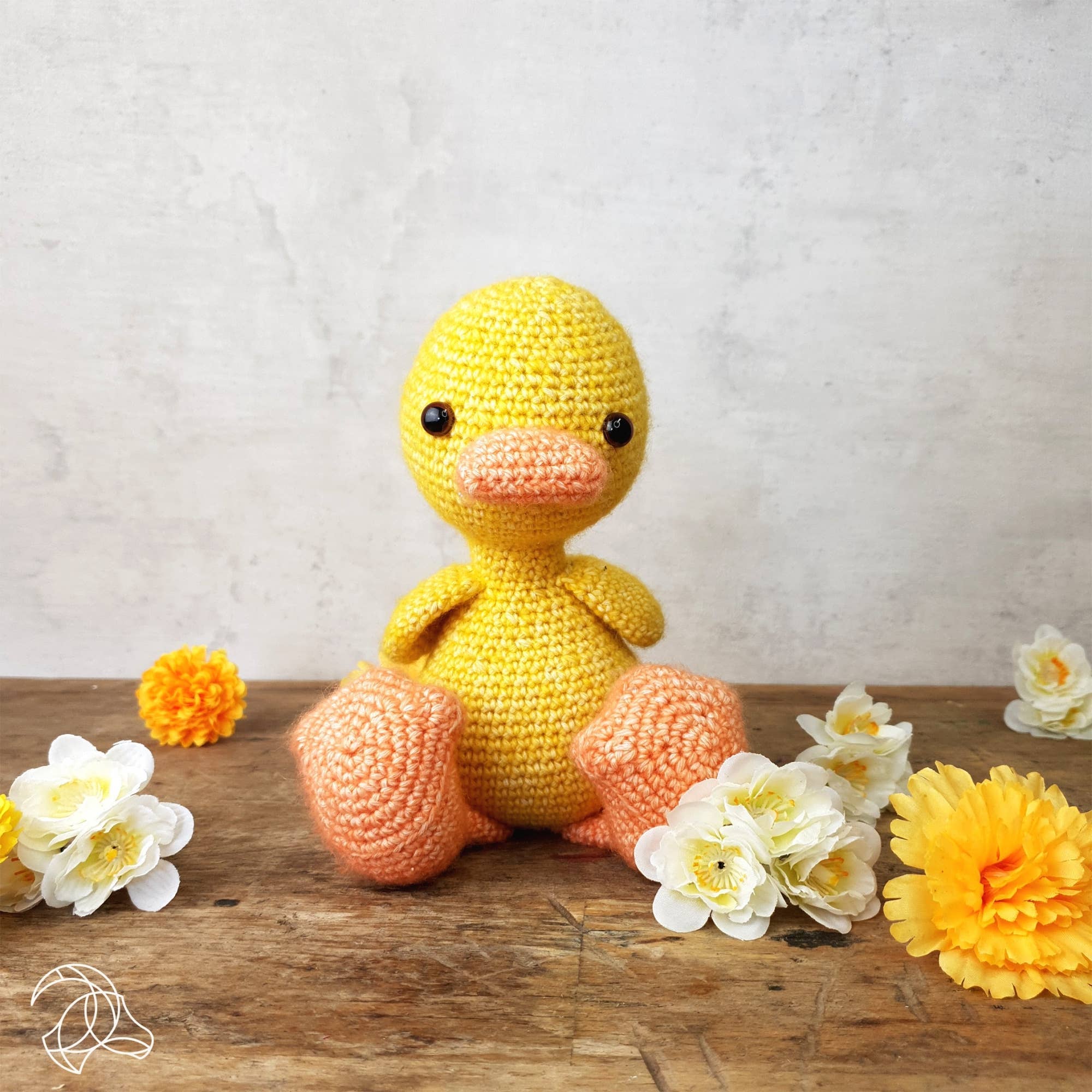 Crocheted yellow duck toy on a wooden surface with flowers