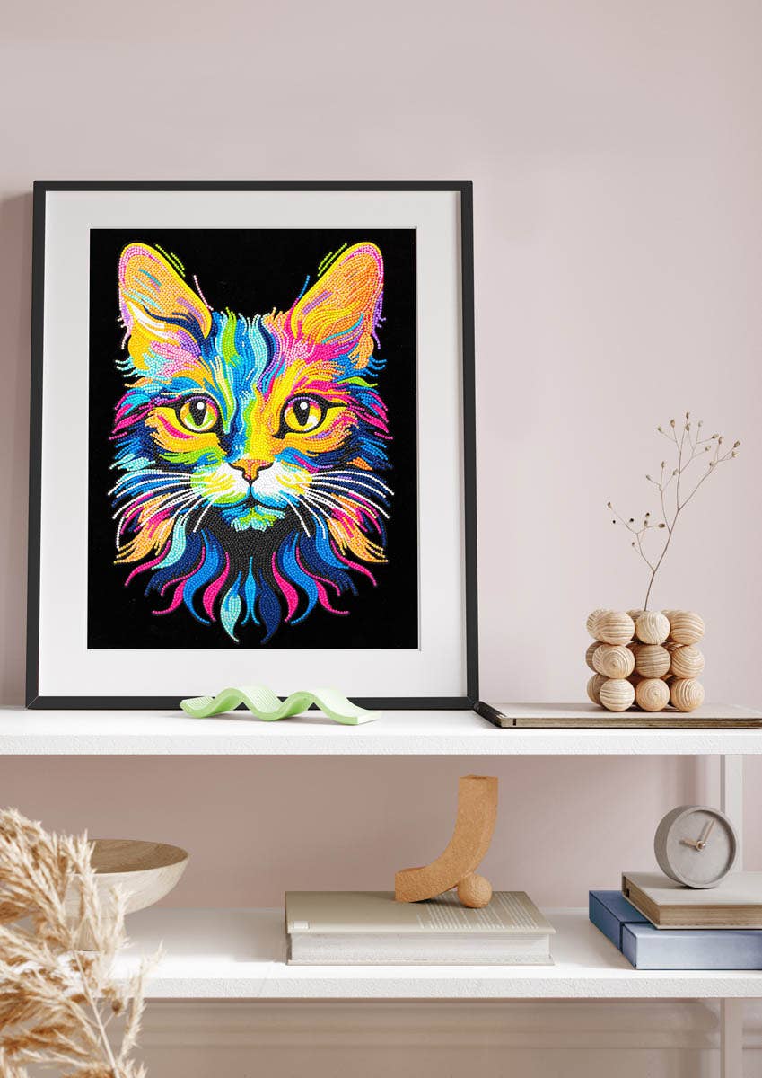 Framed colorful cat painting on a wall above a shelf with decorative items.