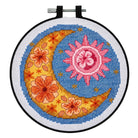 Cross-stitched design of a sun and moon with floral elements in a hoop.