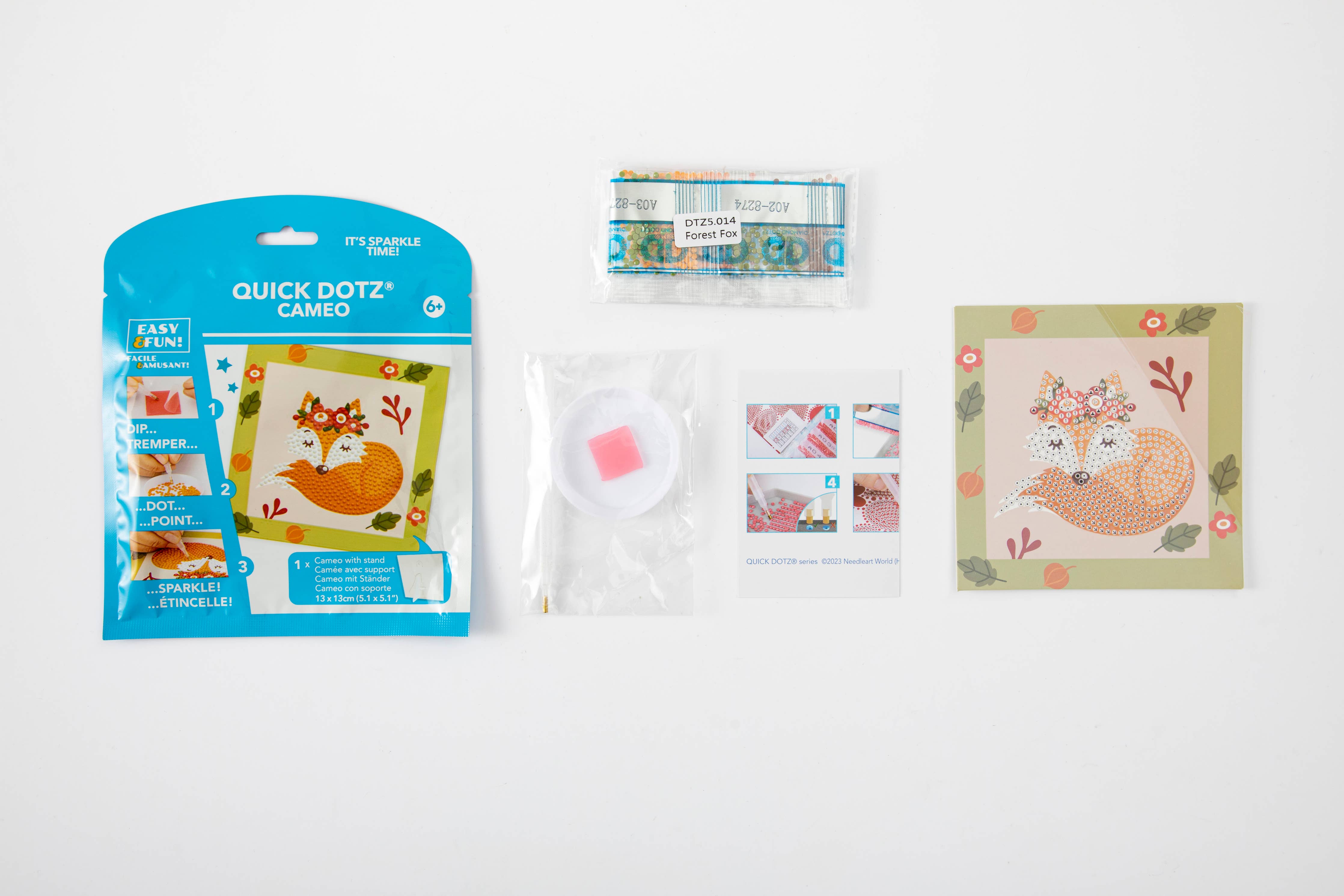 Crafting supplies including a package of Quick Dotz Cameo and a cross-stitch design on a white background.