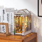 Decorative miniature greenhouse model on a wooden surface with books in the background