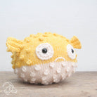 Knitted puffer fish toy on a wooden surface with a light gray background