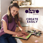 Girl playing with a toy on a table, with 'OKTO' branding in the background.