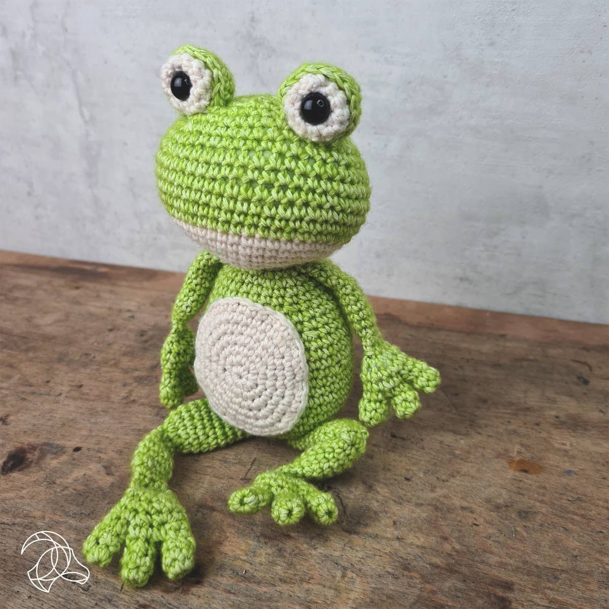 Crocheted green frog toy on a wooden surface with a gray background