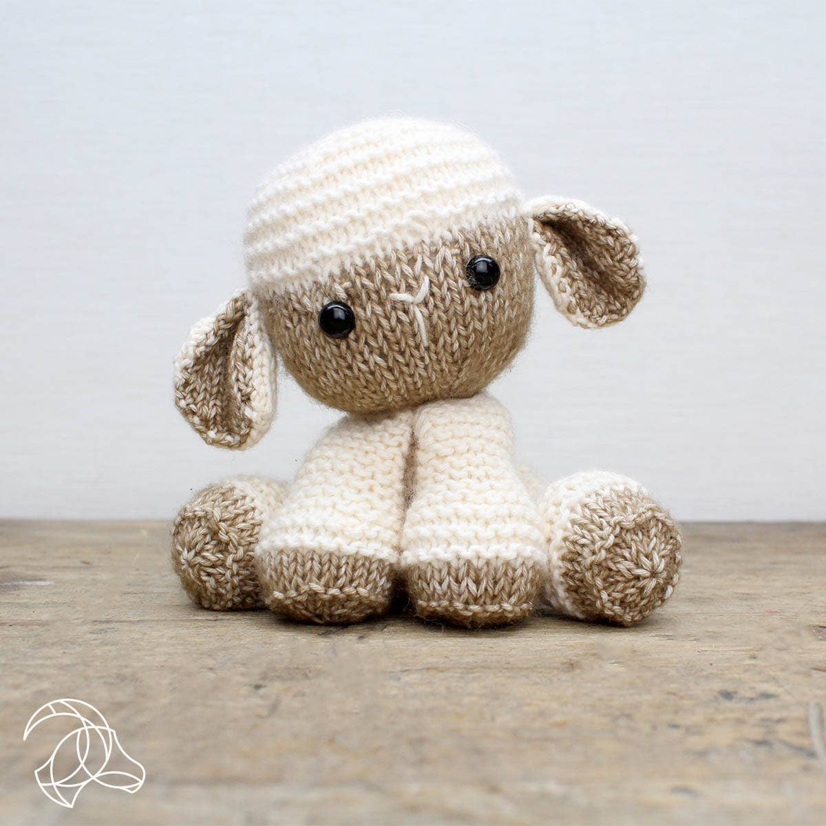 Knitted toy sheep on a wooden surface with a light gray background