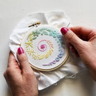 Embroidery hoop with colorful floral design held by a person's hands.