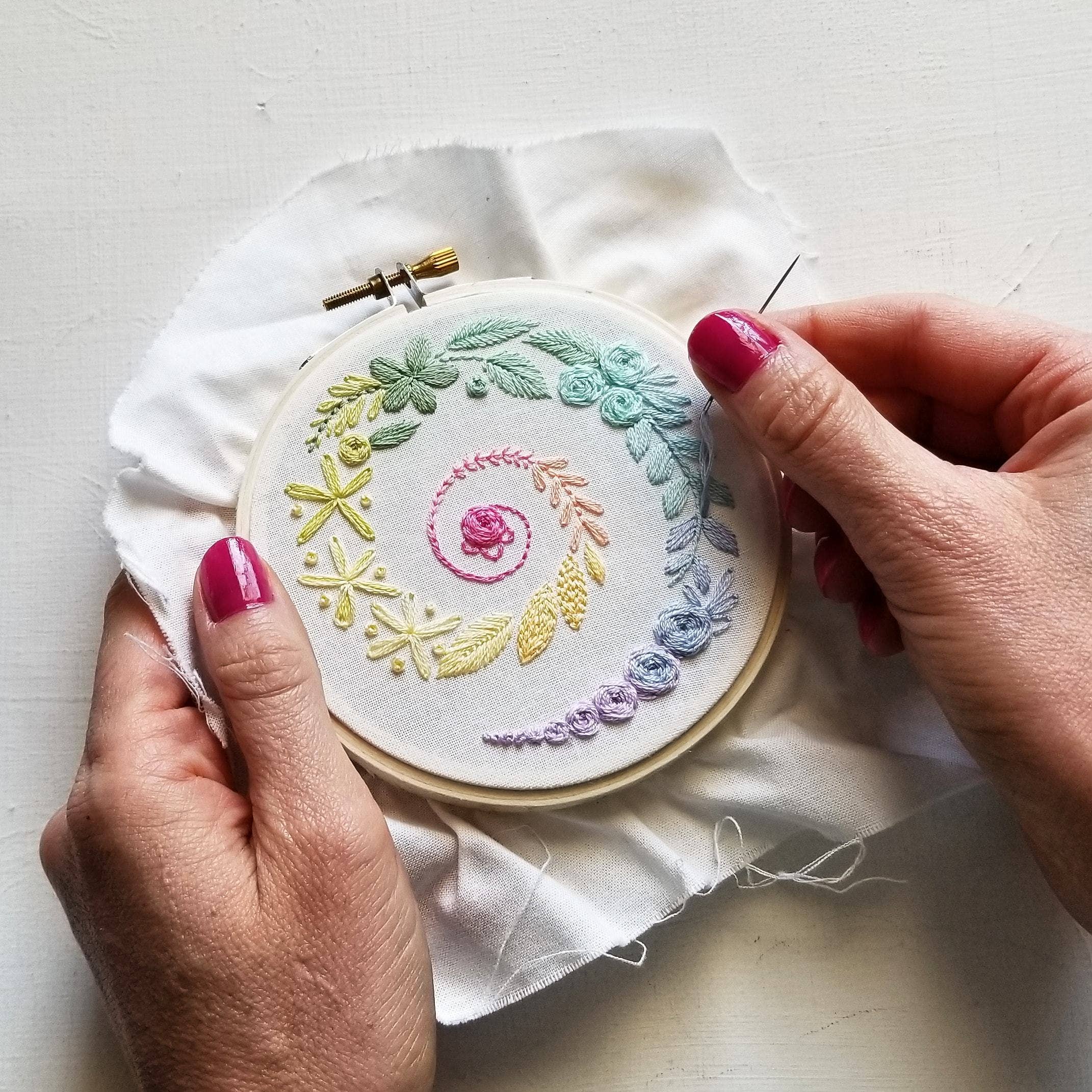Embroidery hoop with colorful floral design held by a person's hands.