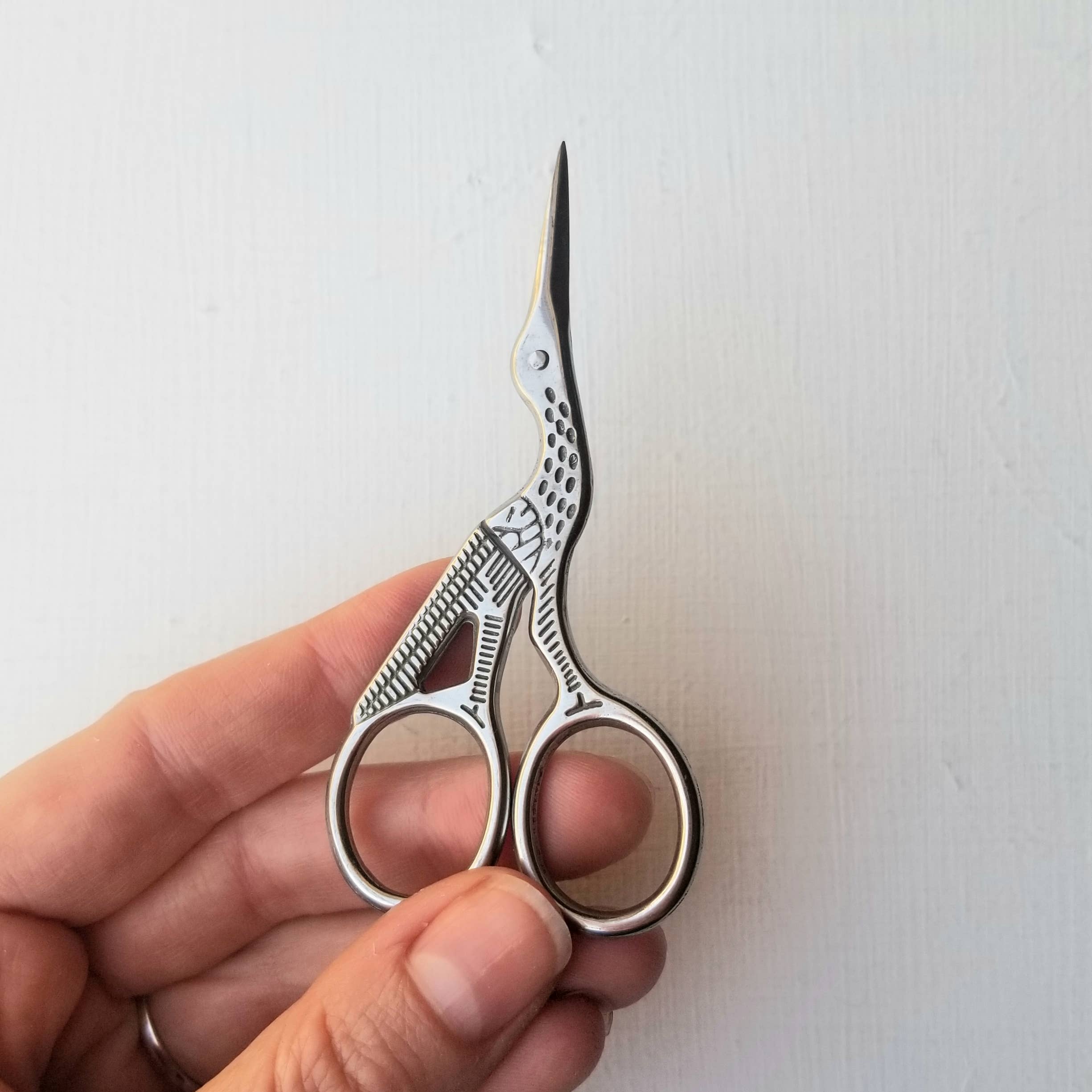 Hand holding a pair of silver scissors against a white background