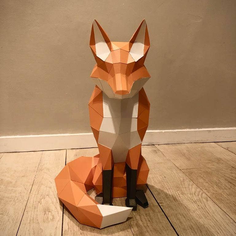 Geometric paper fox sculpture on a wooden floor against a beige wall