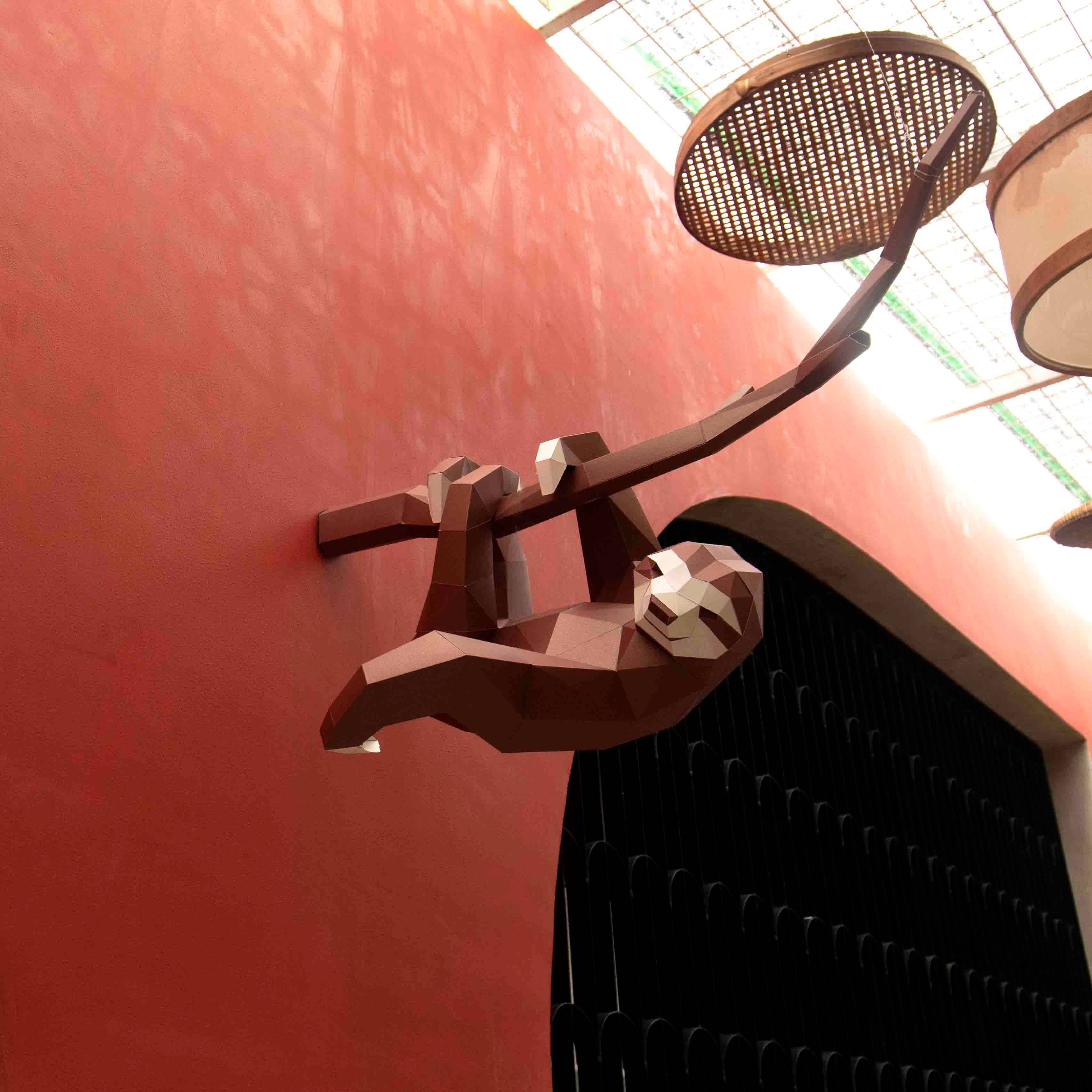 Picture of a sloth figurine on a branch against a red wall