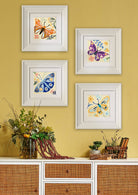 Four framed butterfly artworks on a yellow wall above a wooden cabinet.